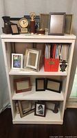 Overall view of bookshelf with frames, books, clock and stationery