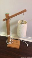 Full view showing wooden base, arm, white cylindrical shade, cord and plug