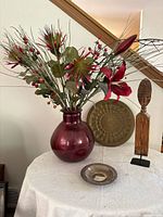 Full lot view showing floral arrangement in red vase, brass plate, wooden figure, pewter bowl