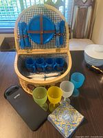 Open basket showing plate, cutlery, mugs, wine glasses, napkins, wine carrier