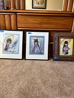 Three framed DeGrazia artworks leaning against furniture