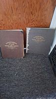 Two cloth-bound atlases standing side by side, brown and grey covers visible