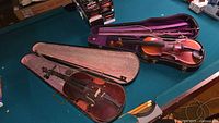 Overview of both violins in open cases with bows on pool table