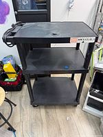 Front view of black three-shelf AV cart on casters