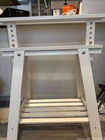 Front view of white adjustable trestle showing top supports and lower slatted shelf