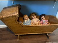 Full view of wooden rocking cradle with three dolls inside