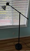 Full view of black pivot arm floor lamp standing by window