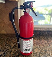 Full view of the Kidde red fire extinguisher on countertop showing hose, gauge, handle and bracket