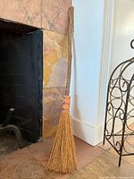 Full view of broom showing straw bristles, decorative binding, and branch handle