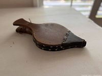 Side view of wooden fireplace bellows showing leather gusset and brass studs