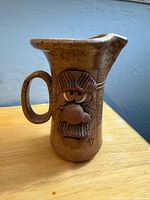 Front of stoneware mug showing folk art face and handle