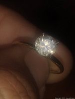 Close-up of ring held between fingers showing clear round stone and gold band