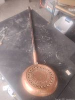 Full view showing entire copper pan with wooden handle on work surface
