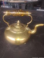 Full left view of polished brass teapot showing amber glass handle, spout, lid finial and feet