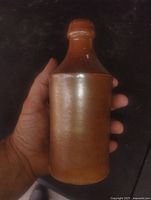 Front view of brown stoneware bottle held in hand