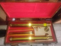 Open wooden box showing all brass telescope components in red felt interior