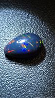 Pear cabochon black opal on textured background showing multicolor flashes