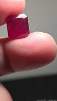 Ruby held between fingers showing deep red color and emerald cut face