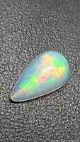 Pear cabochon Ethiopian opal on textured black surface showing green and red flash
