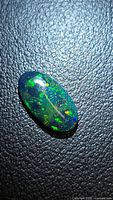 Oval cabochon opal showing multicolor flash on textured background