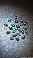 Group of approx. 24 oval black opal cabochons on textured surface