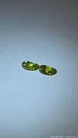 Two oval cut apple-green Peridot gemstones on neutral background