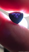 Trillion-cut dark purple spinel held between fingers under light showing table and crown facets