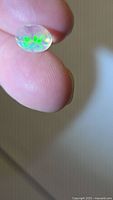 Oval faceted opal showing green flash held between fingers