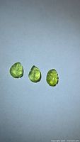 Three lemon-lime leaf-cut tourmalines on neutral background