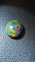 Top view of round black opal showing multicolored fire and green section