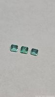Three loose emerald-cut green gemstones on neutral background