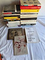 Full view of stacked hardcover and paperback books showing quantity and variety; three additional books laid flat in front