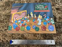 Presentation folder with Beauty and the Beast The Enchanted Christmas artwork and ruler for scale