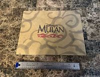 Front of tan envelope showing Disney’s Mulan logo with dragon graphic, ruler for scale