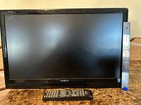 Front view of Insignia TV with remote, size reference by ruler