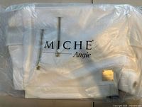 Front view of white Miche Angie Prima shell showing gold zippers, logo plate, packaged strap