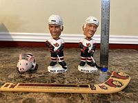 Front view of both bobbleheads with plush pig, mini stick and ruler for scale