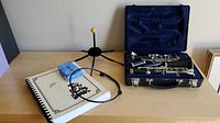 Clarinet case open with disassembled clarinet, stand, reeds, strap, book on tabletop