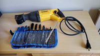 Corded DeWalt reciprocating saw with attached power cord and blade roll opened to show blades
