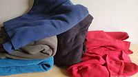 Stack of folded polar fleece pieces in blue, black, charcoal, teal and red