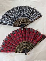 Two lace folding fans displayed open, black fan above red fan