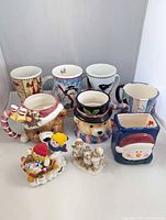 Group view of six mugs, square Santa vase, two resin figurines