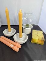 Overview of pair Poole ceramic holders with yellow tapers, glass globe votive holder on ceramic base with green votive, pack of Claire Burke tealights, two peach taper candles