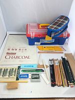 Entire lot laid out: paper pad, toolbox, pouch, pencils, sticks, erasers, tools