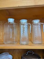 All three glass jugs on shelf showing sizes and lids