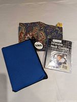 All three travel accessories laid out: blue poncho pouch, paisley shoe bag, sealed inflatable neck cushion