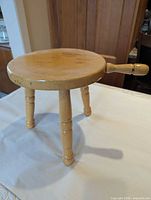 Top view of wooden milking stool showing round seat and side handle