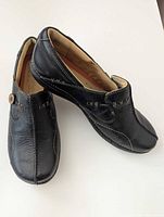 Side and top view of both loafers showing leather texture, stitching, and button accent