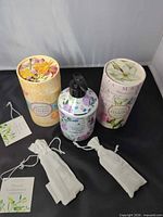 Two cylindrical Crabtree & Evelyn boxes, Avery Lane pump soap bottle, two cloth pouches on black surface
