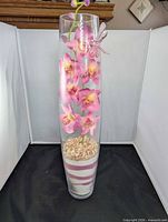 Full view of tall glass vase with orchid arrangement and sand layers